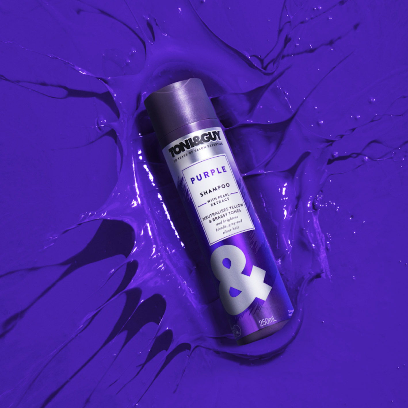 Image of Toni & Guy Purple Shampoo bottle placed on a vibrant splash of purple liquid