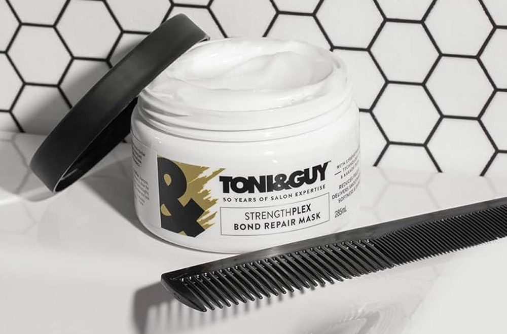 Toni & Guy StrengthPlex Bond Repair Mask placed on a bathroom counter with a comb, illustrating 'what is a hair mask' and its role in repairing and nourishing hair.